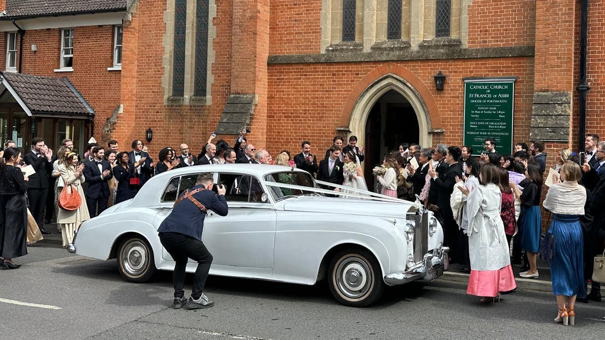 Classic Rolls-Royce silver Cloud sourrounded by wedding guests in front of church