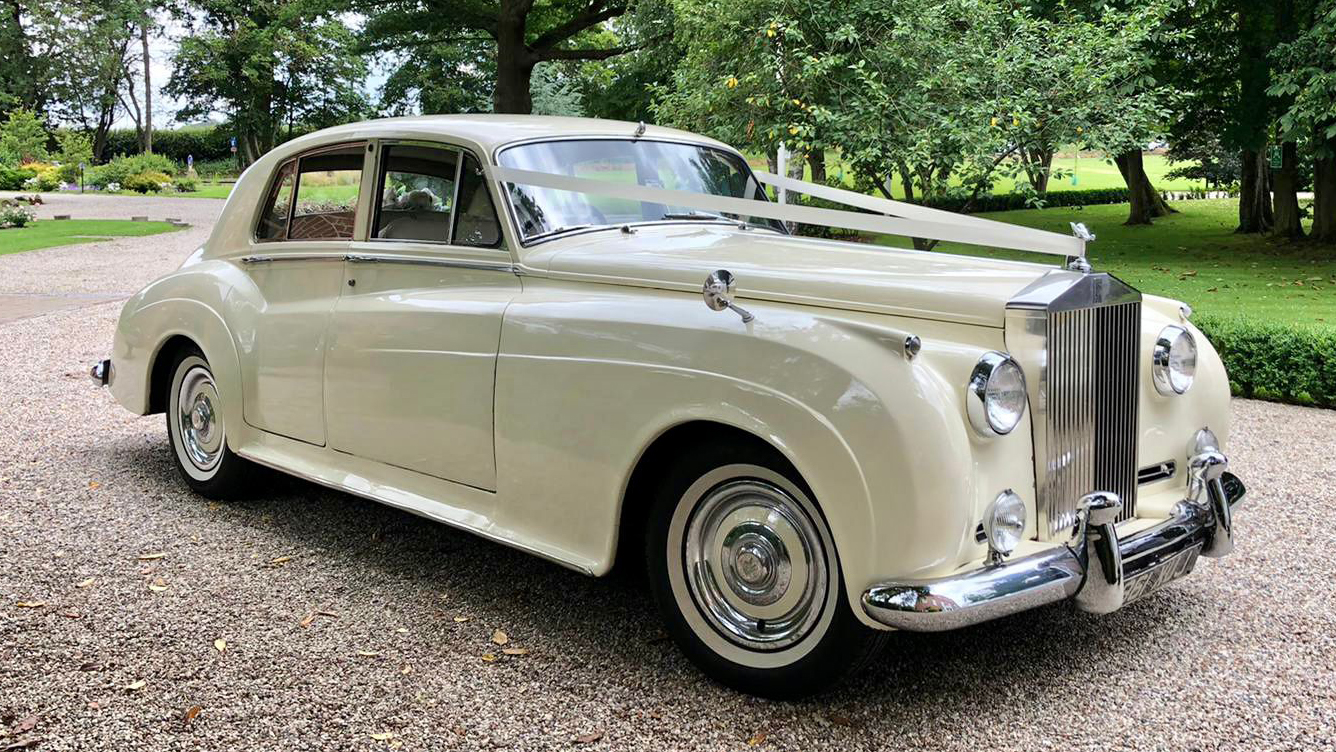 front side view of Classic Rolls-Royce decorated with Ivory Ribbons in a Park with Green Trees in the Background