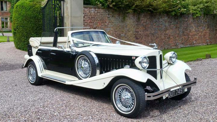 Side view of Black & Ivory BEauford Convertible in White with Black Sides decorated with white ribbons in front of a wedding venue