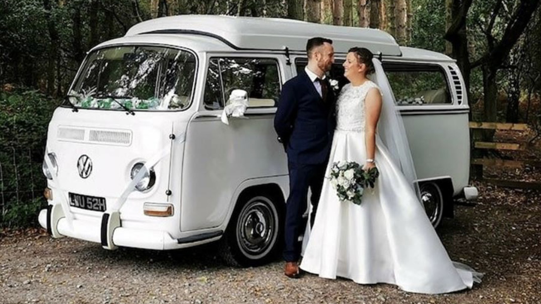 Bride and Groom standing in front of a White classic VW Campervan. Bride is holding her wedding bouquet in her left hand