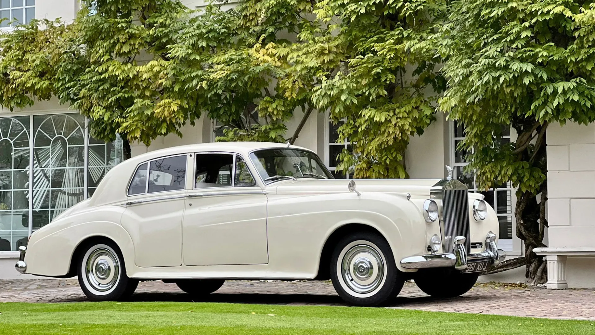 Side view of ivory Classic Rolls-Royce Silver Cloud in front of venue with Green ivy covering the wall
