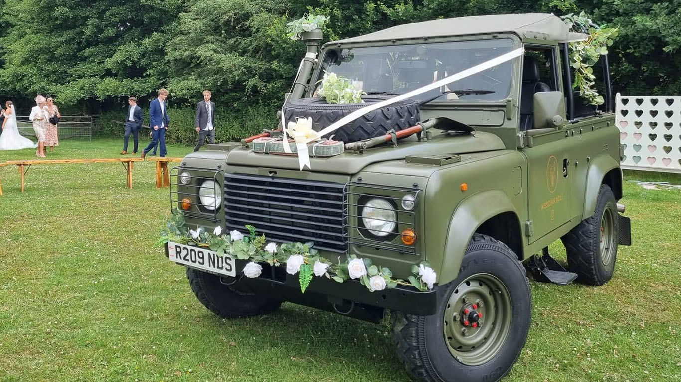 Military Landrover in Khaki Green decorated with white Ribbons and flowers on front parcel sheves.