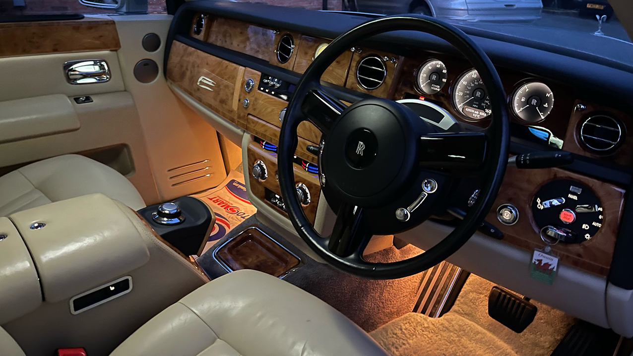 Front passenger seating area showing the cream leather interior and wooden dashboard. Under dashboard light on