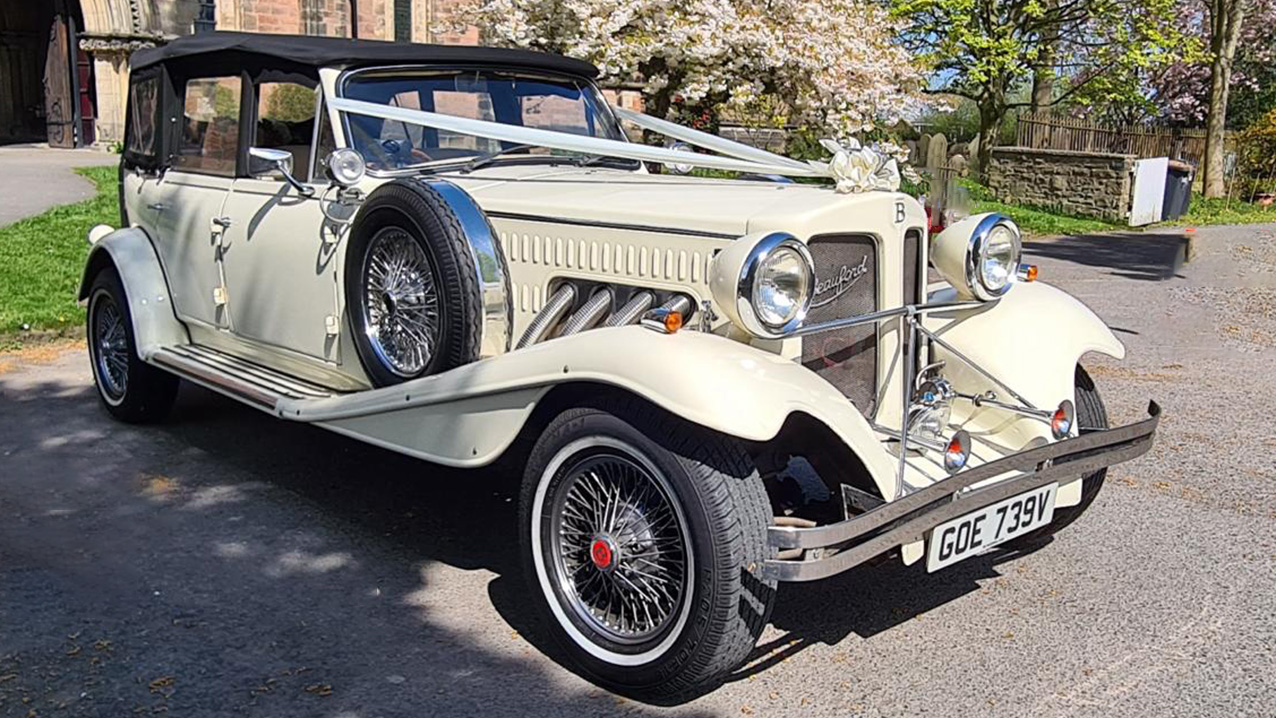 Right view of Beauford Convertible with Roof Up, decorated with White ribbons accross the bonnet in front of a wedding venue