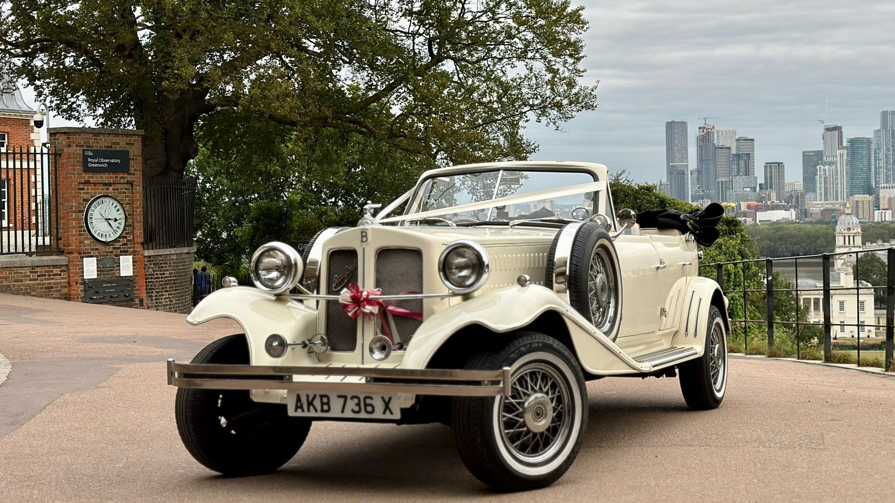 Front Side View of Vintage Beauford with convertible roof down decorated with white ribbons opn top of a hill showing City of London in the Background