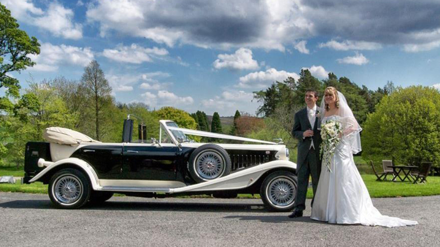 Bride and Groom stangin in front of Beauford Convertible.