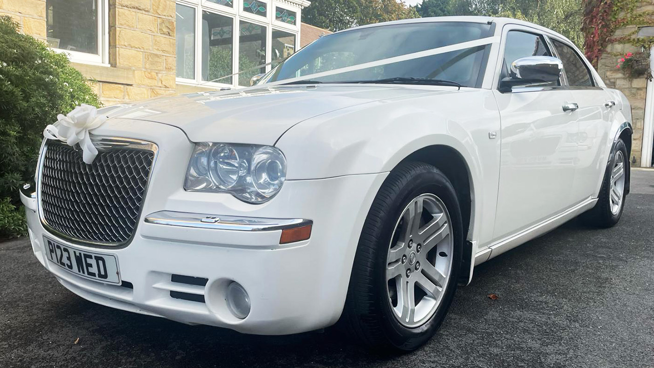 Front Left view of a White Chrysler 300c Saloon with White ribbons and bow across the front bonnet