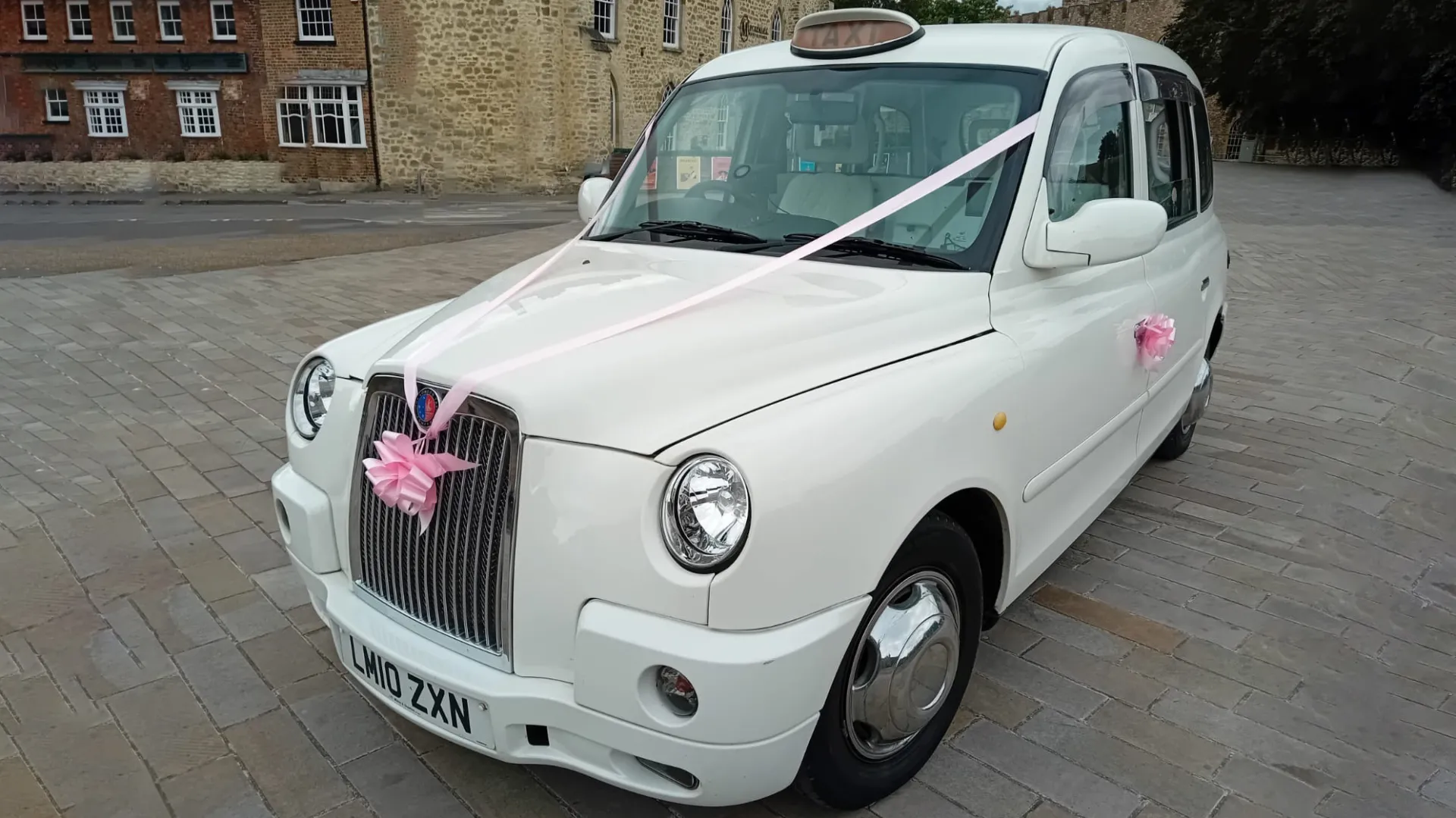 Side front view of White Modern Taxi Cab decorated with pink Wedding ribbons and bow
