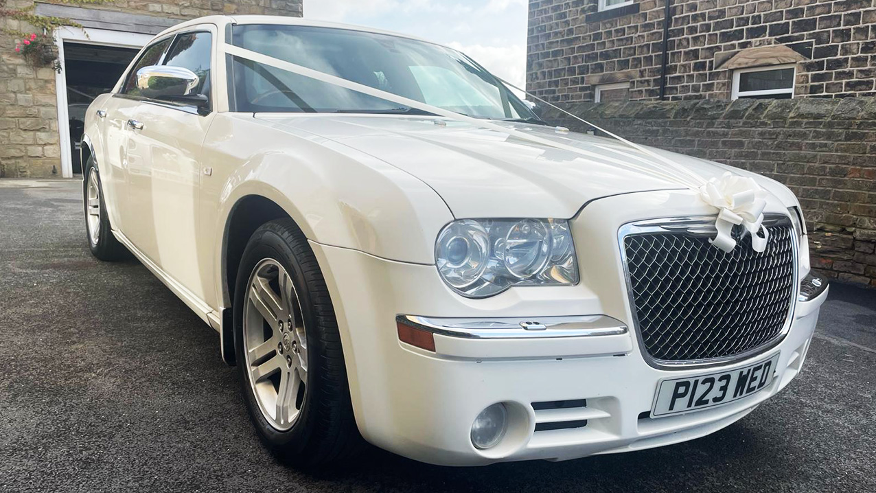 Front view White Chrysler 300c Saloon with White ribbons across the front bonnet outside a house waiting for Bride