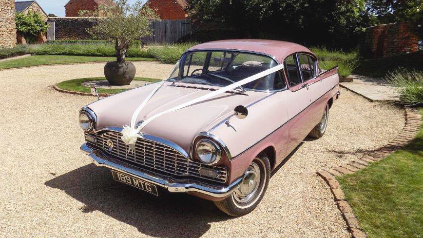 Classic Vauxhall Cresta in Pink decorated with White Ribbons in front of a wedding venue