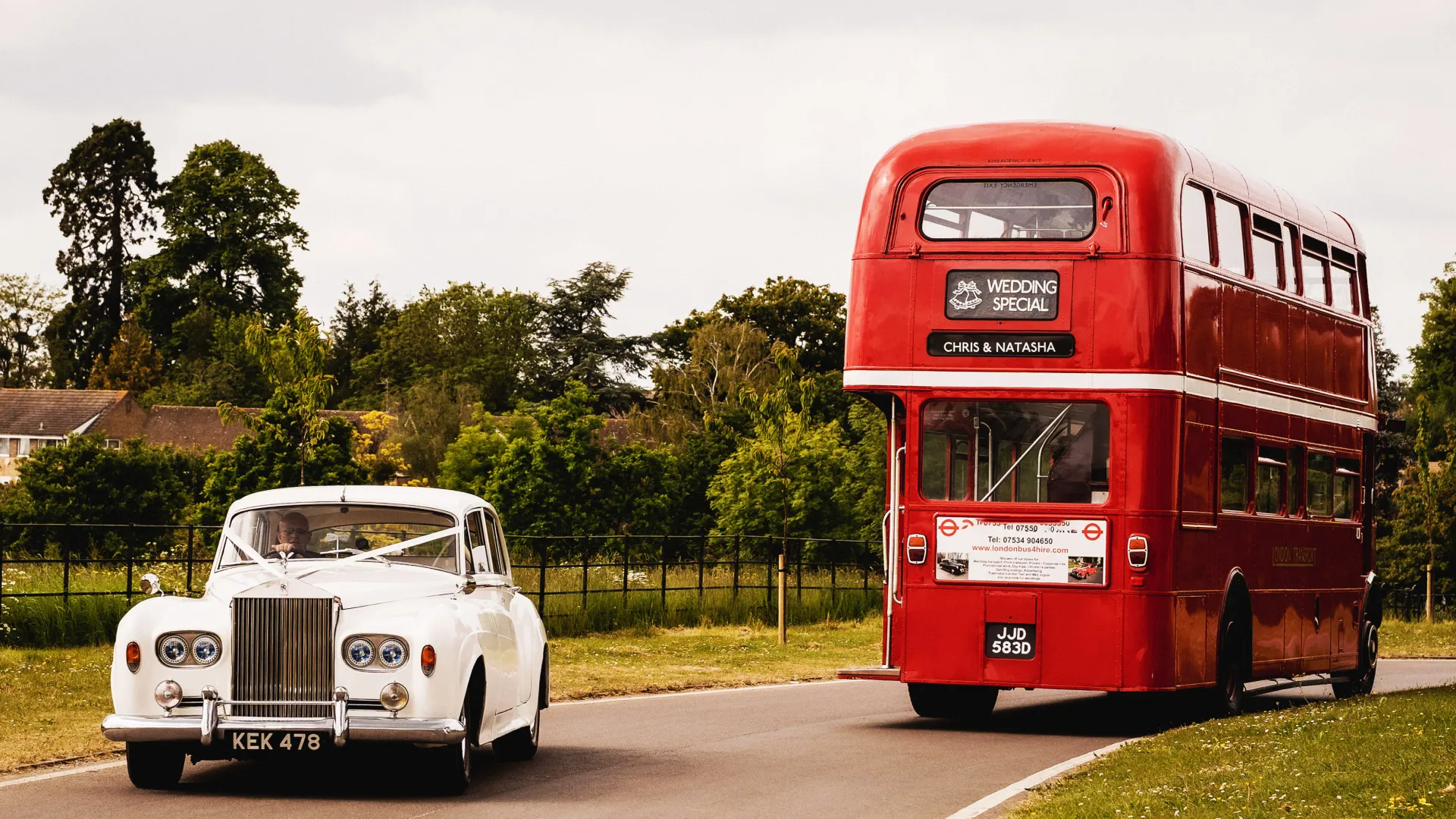 White Classic Rolls-Royce Silver Cloud decorated with wedding ribbons entering a wedding venue while a Double Decker Red Routemaster is leaving