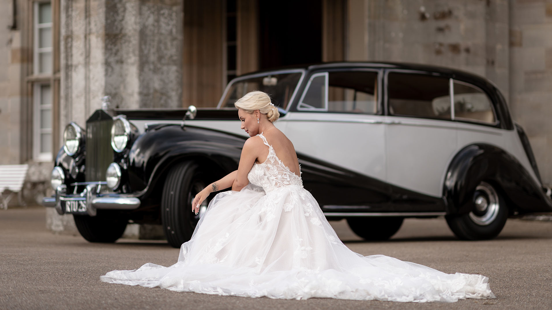Bride wearing a large white dressed seating in front of a Classic Rolls-Royce Limousine