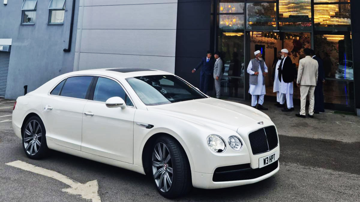 Side view of White Bentley Flying Spur in front of a wedding venue in Manchester with Wedding Guests in the Background