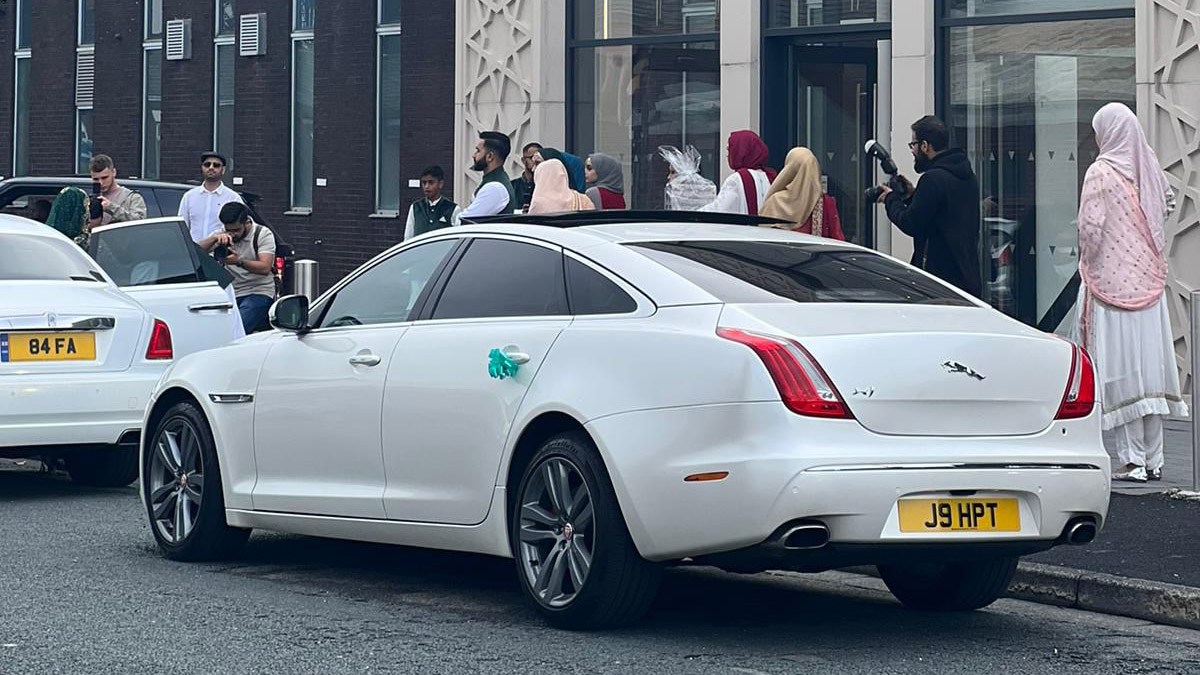 Rear view of White Jaguar in front of wedding venue. Wedding Guests can be seen in the background
