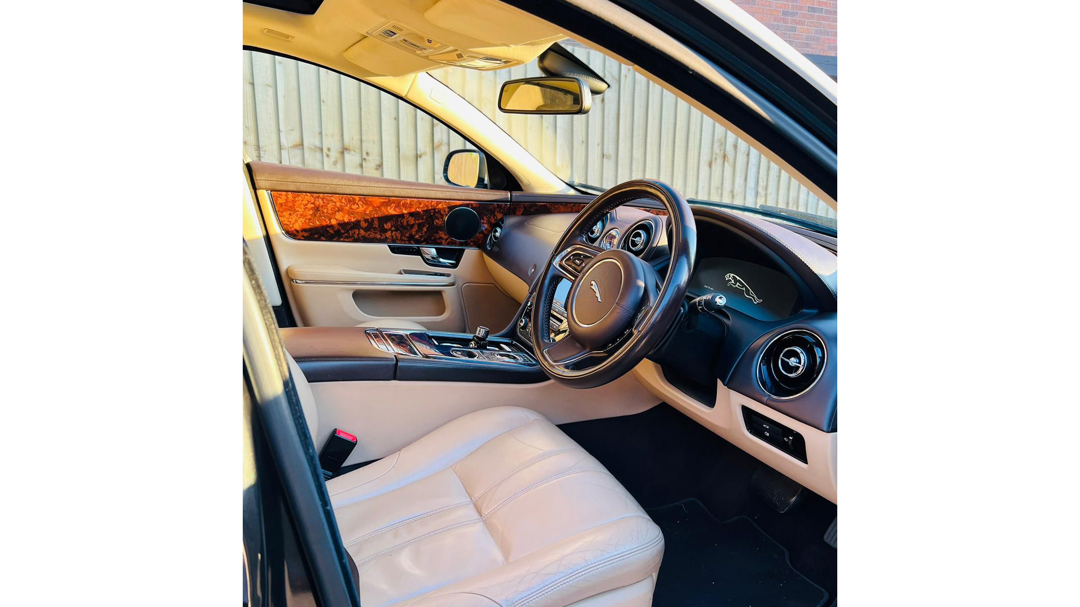 Front seating area in a White Jaguar showing the Cream Leather interior, Steering wheel and wood on top of the door cards.