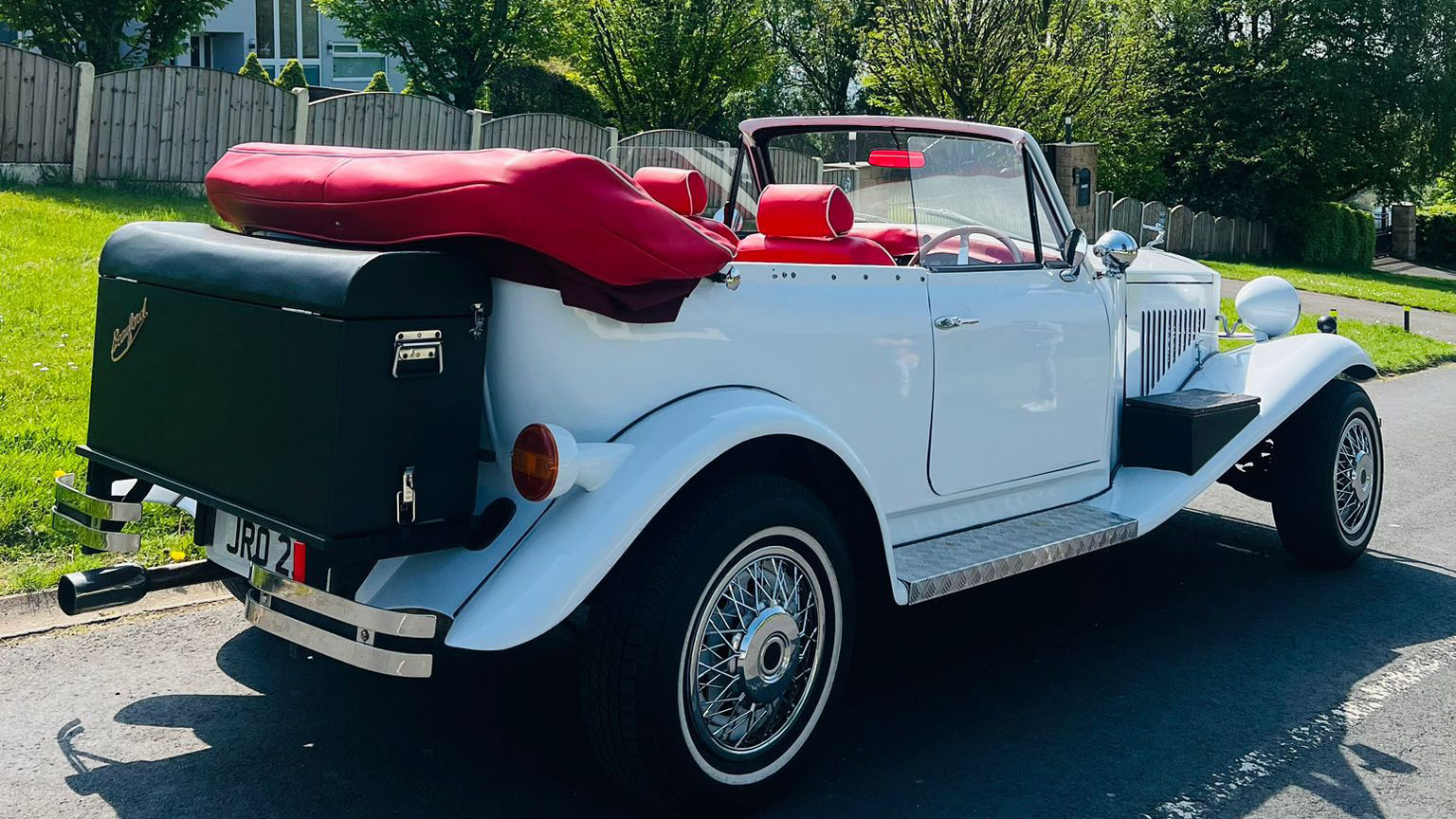 Right side view of White Beauford with roof tucked away in a red cover and black picnic trunk at the rear of the vehicle