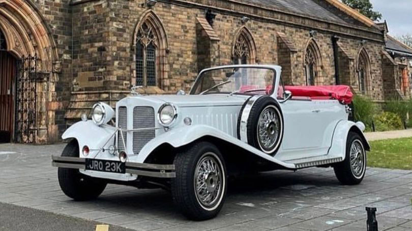 Front Left Side View of White Beauford Convertible with mounted spare wheel on left side in front of church in Manchester