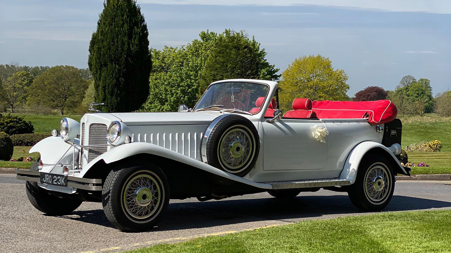 Front Side View of White EBauford Convertible with roof down showing the Red Leather interior and Mounted Spare wheel on left skirt of the vehicle
