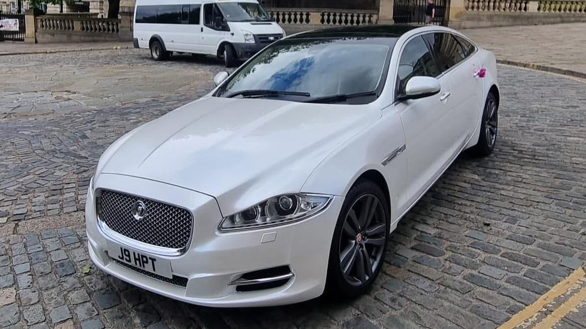 Left Front Side view of White Jaguar XJ on a paved street