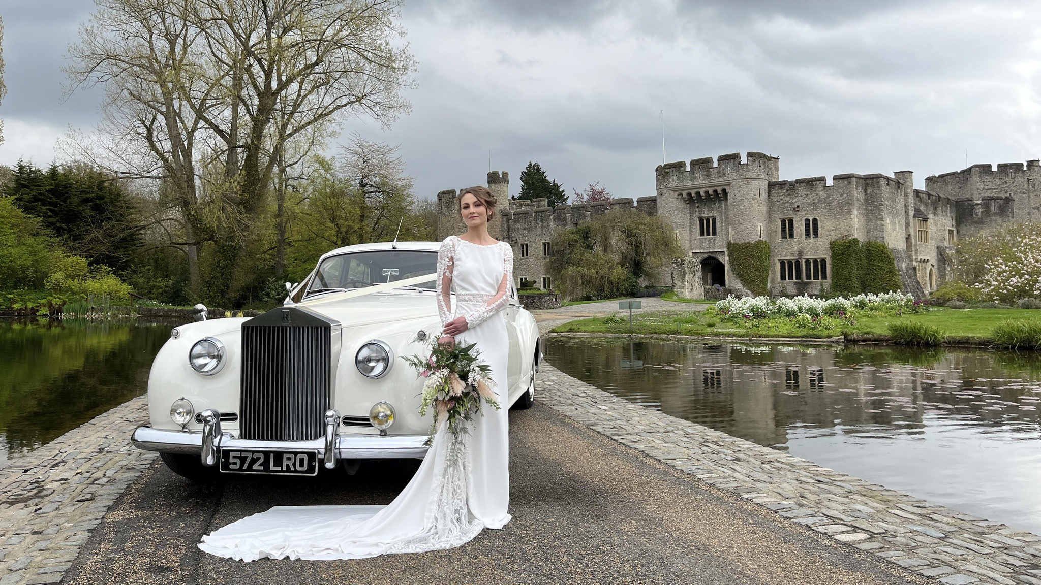 Classic Rolls-Royce Cloud in front of Allington Castle in Kent with bride wearing a white dress and holding a bridal bouquet in front of the vehicle.