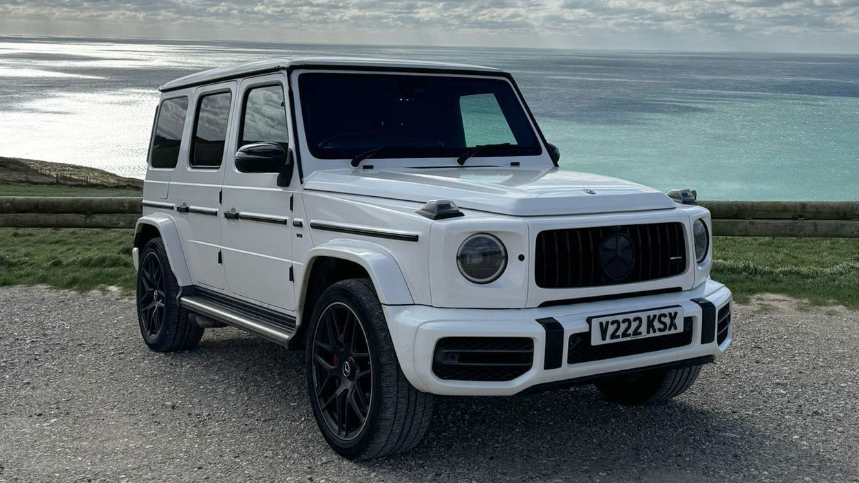 Front side view of White Mercedes G-Wagon on top of a cliff with view of the sea in the background