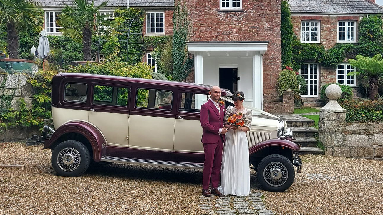 Bride and Groom in front of a Ivory and Burgundy Bramwith Limousine. Bride wears a white dress and Groom wears a matching burgundy suit
