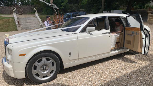 Rolls-Royce Phantom decorated with ribbons with rear door open showing bride seating inside the vehicle