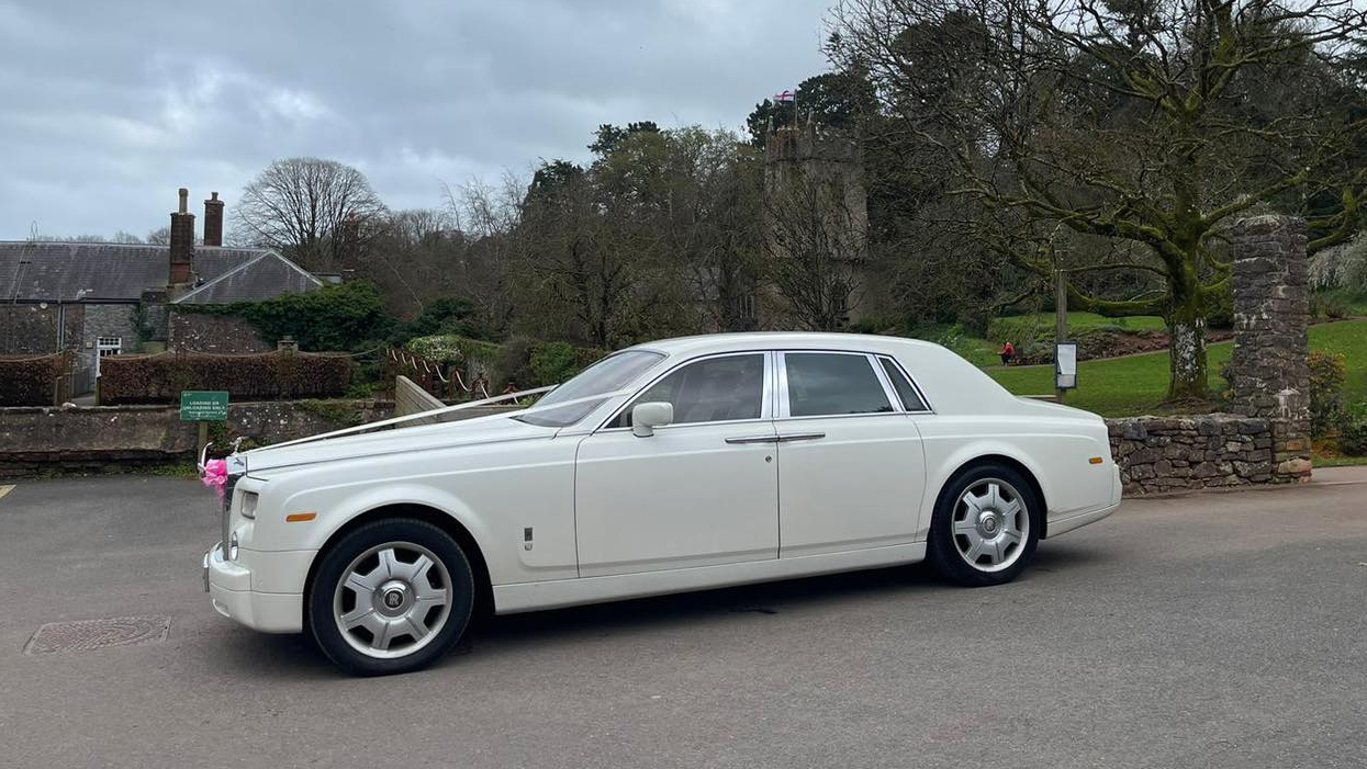 Left view of white Rolls-Royce phantom with white ribbons and pale pink bow in front of the vehicle
