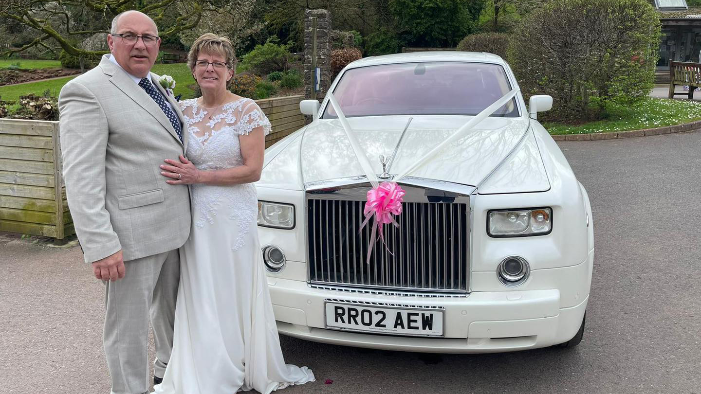 Bride and groom standing in front of the White Rolls-Royce pahntom decorated with Pink bow