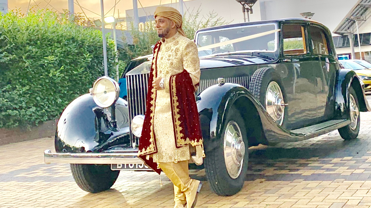 Asian groom standing in his traditional wedding cloth in front of the vintage Rolls-Royce Phantom
