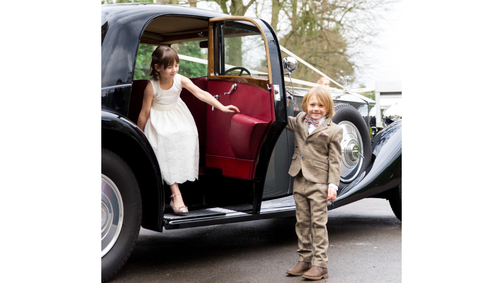 Boy opening the door to the vintage Rolls-Royce to let a little flower girl out of the vehicle