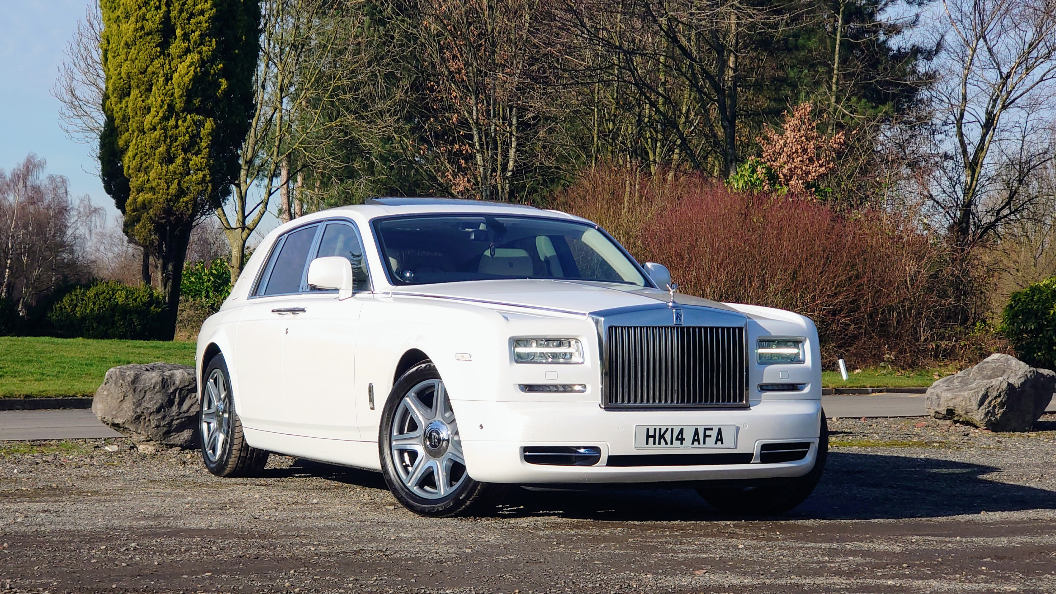 Modern White Rolls-Royce Phantom in front parked in a park with autumn colours.