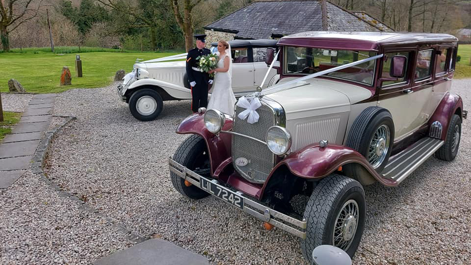 Bramwith Limousine and a Beauford Convertible decorated with matching white ribbons on wedding duites. Bride and Groom are standing in the middle of the vehicles.