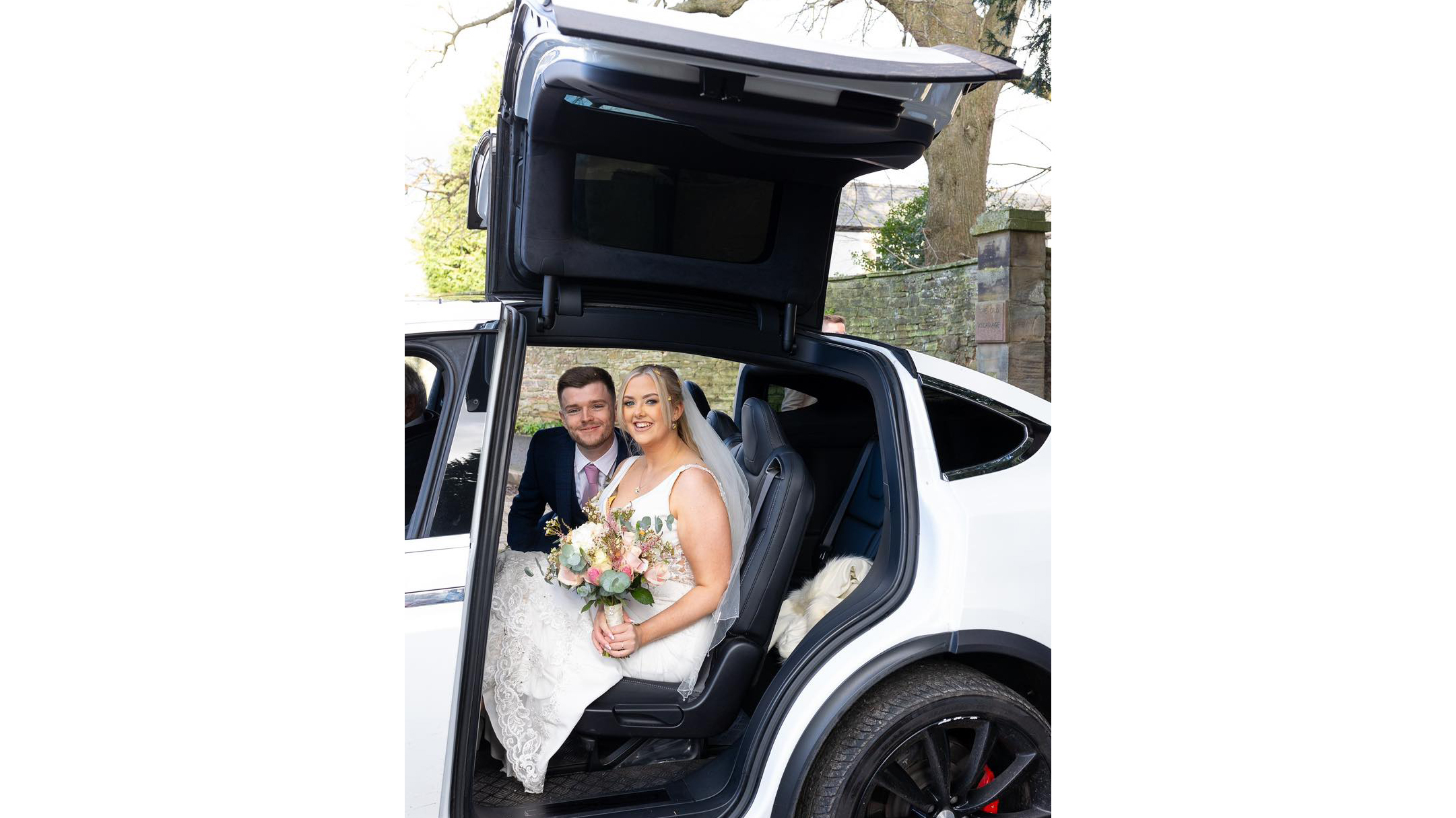 Bride and Groom seating inside a White Tesla X with open Gull-wings.