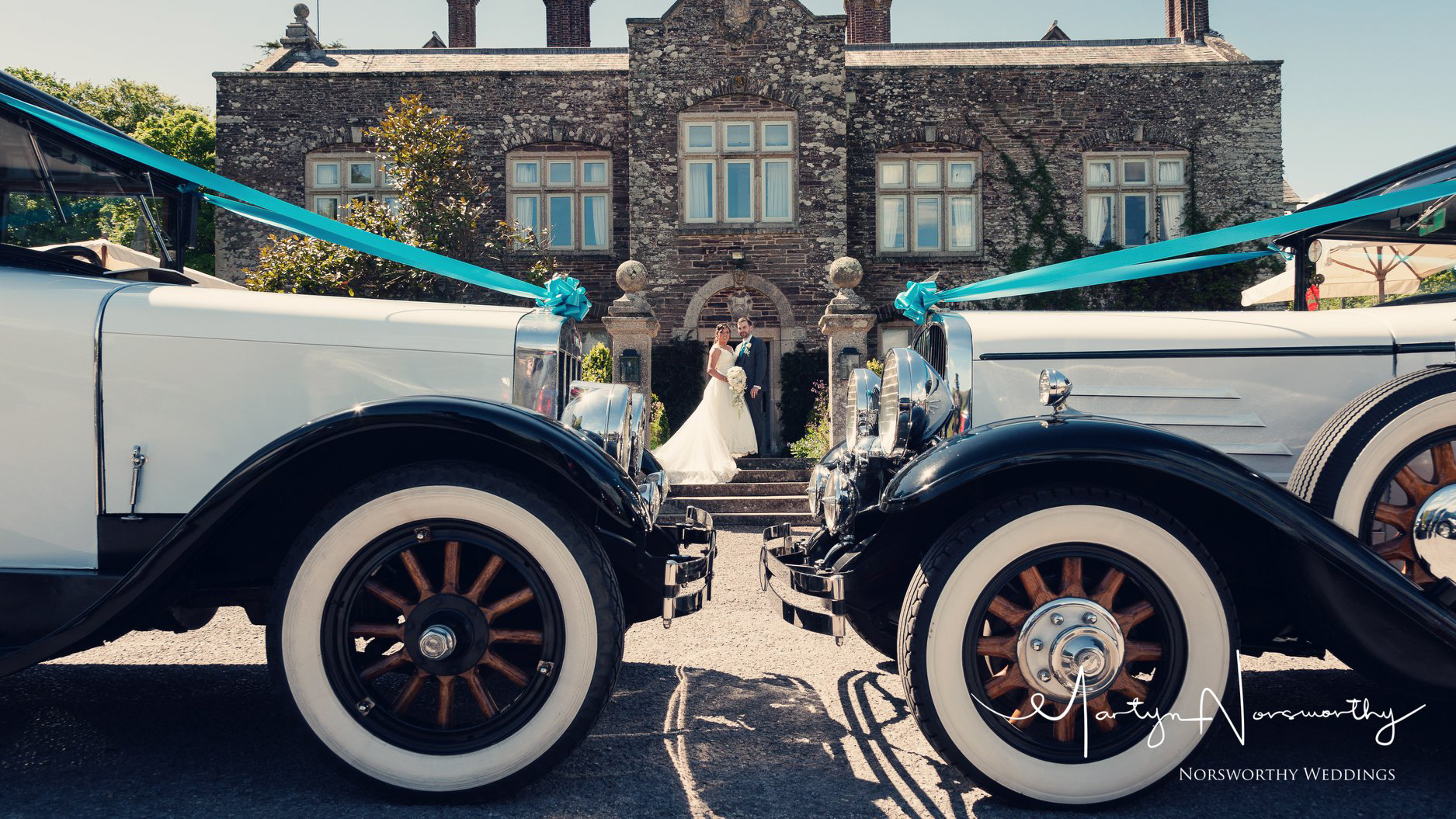 Front section of matching vintage wedding cars with Bride and Groom in the Background