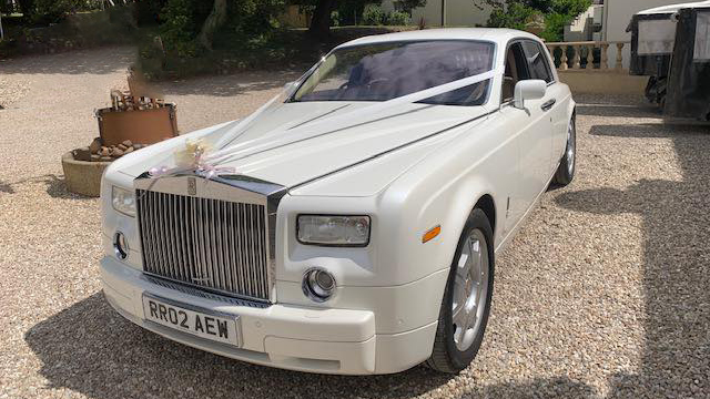 Front view of White rolls-Royce decorated with ivory wedding ribbons