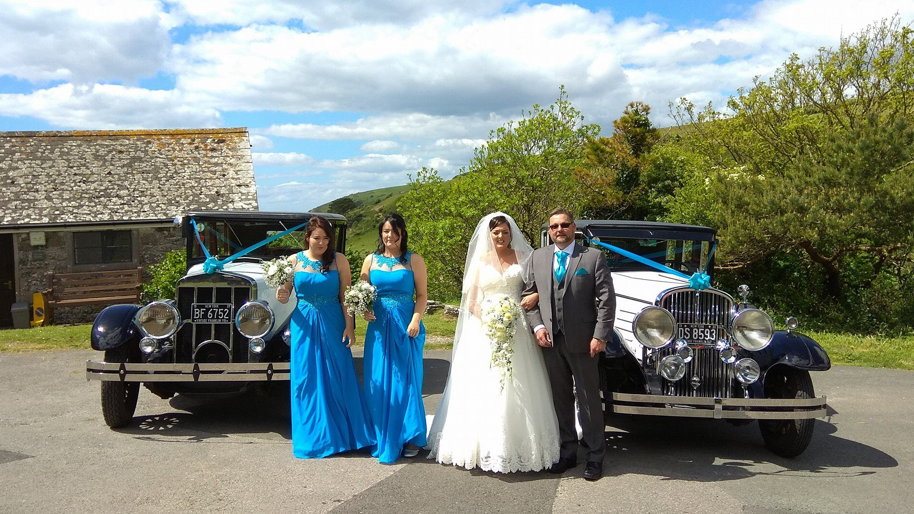 Pair of identical american vintage car with matching Turquoise blue ribbons. Bride, Groom and two bridesmaids standing in front of the vehicles