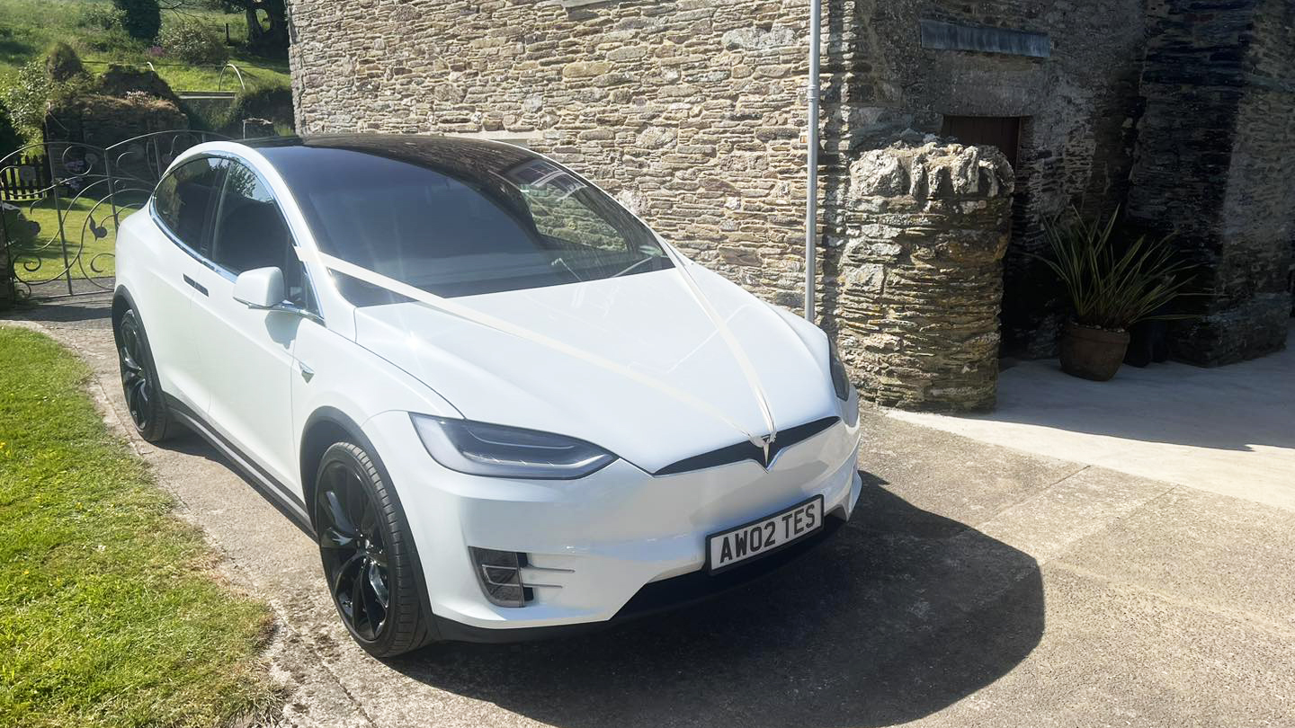 Front Side view of Tesla X in white with white ribbon across its bonnet