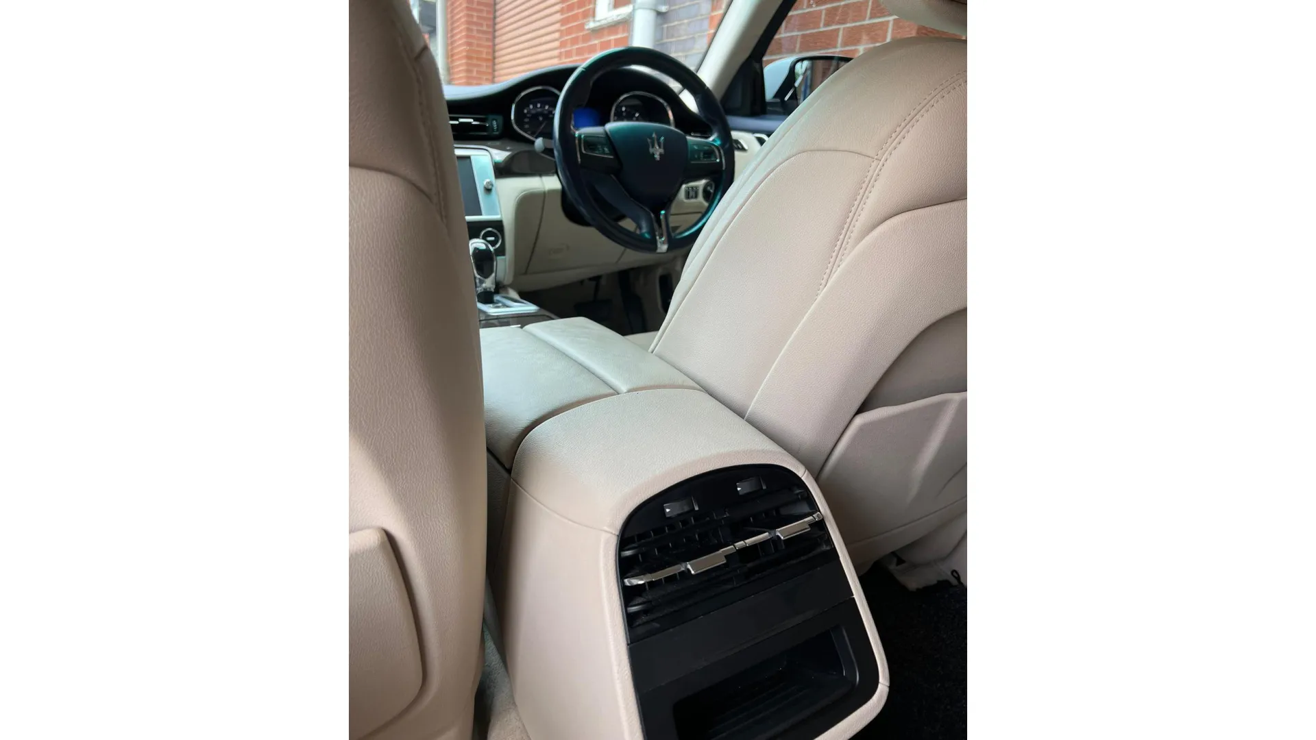 front view from the rear passenger seats of cream leather interior, steering wheels and dashboard.