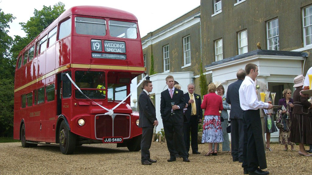 Routemaster Bus decorated with with ribbons and bow. Wedding guests around the bus