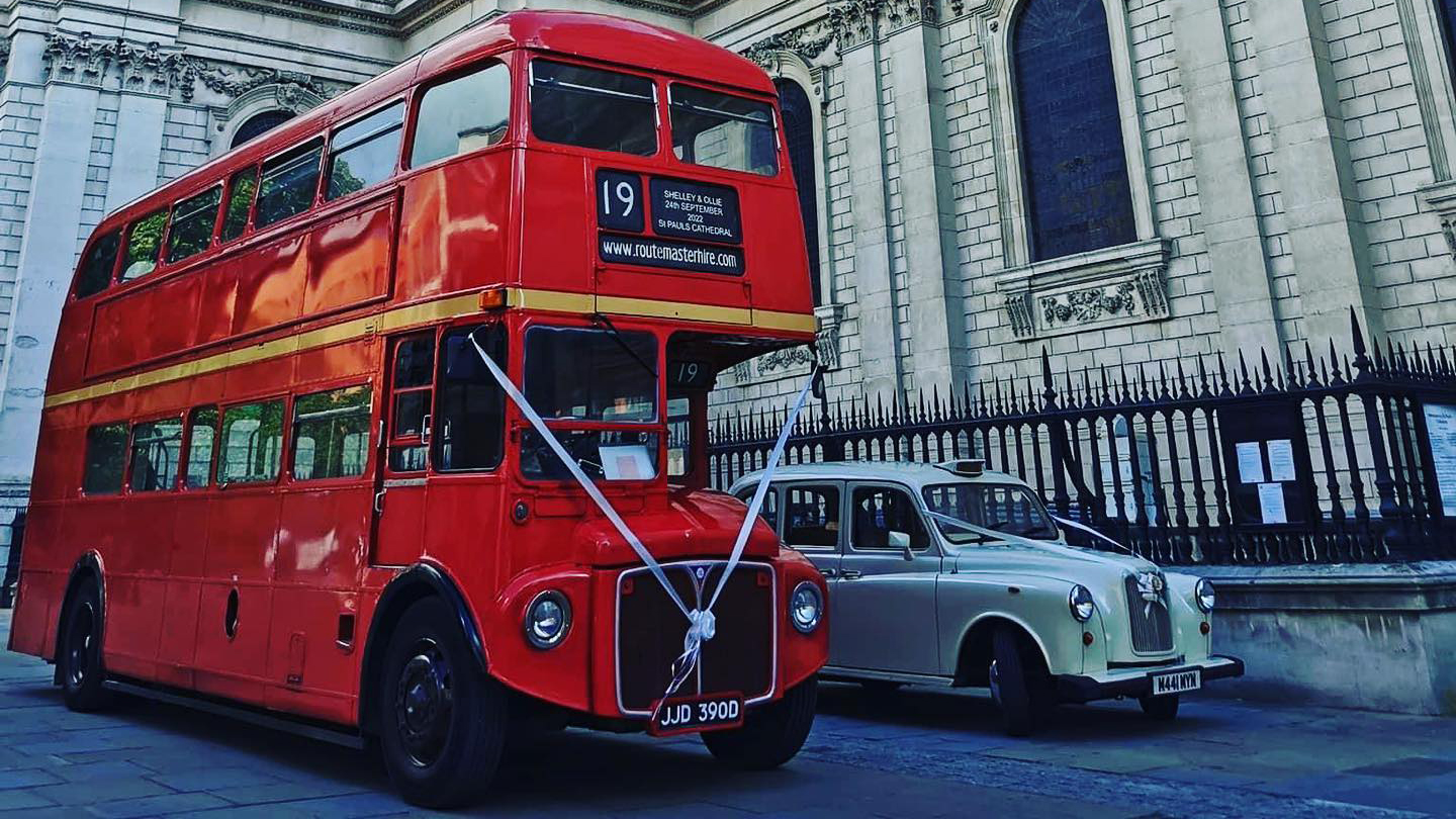 Red Routemaster bus and a classic london Taxi Cab parked side-by-side decorated with matching white ribbons