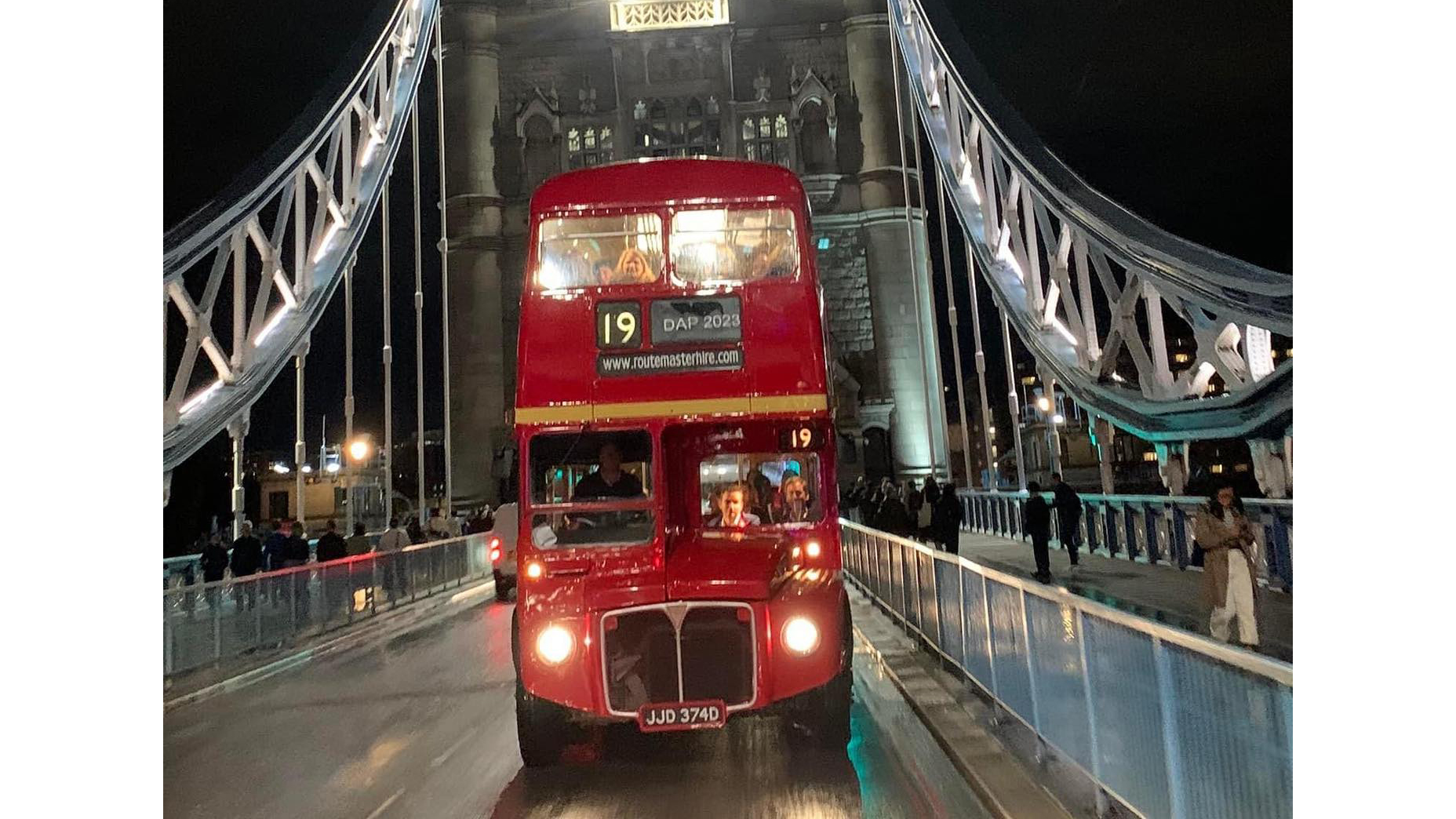 Red Routemaster bus with lights on being driven on London Bridge at night