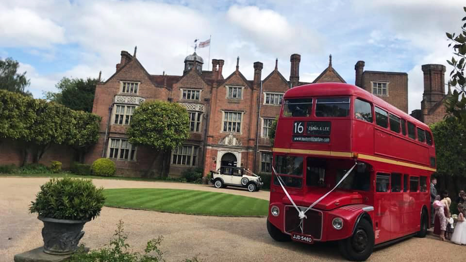 Double Decker Red Bus with wedding guests exiting the bus. Vintage car can be seen in the background in front in front of the wedding venue