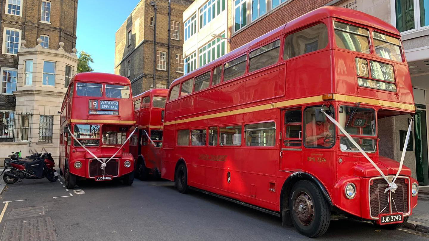 three Routemaster busesparked in the Street of London with matching white ribbons