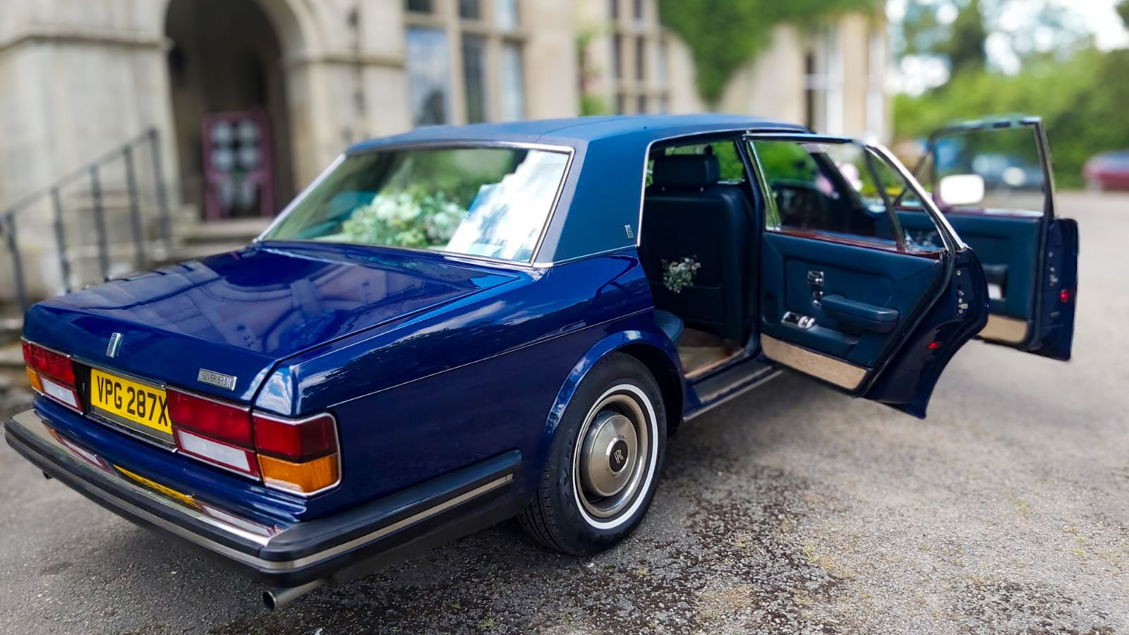 Side rear view of blue classic rolls-royce with both front and rear doors open showing blue interior on door panels
