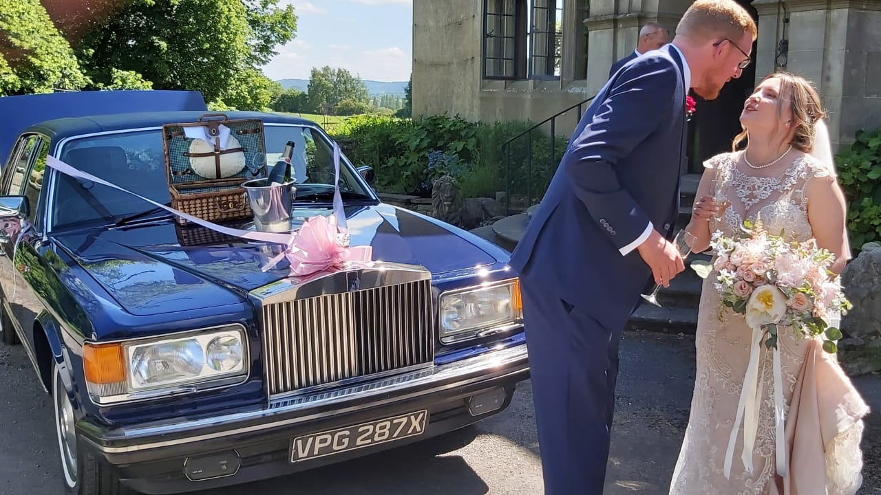 Bride and Groom in front of a classic roills-royce smiling at each others.