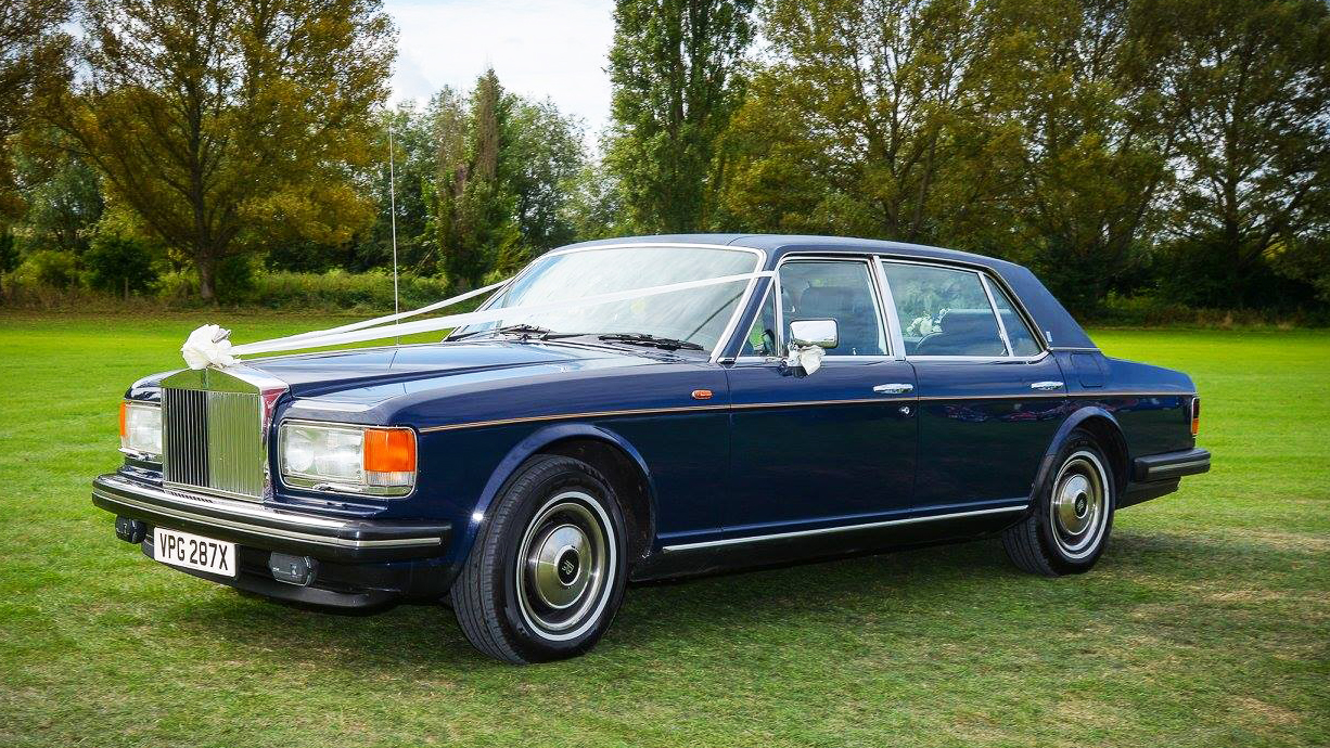 Front side view of Blue Rollsyce silver Spur decorated with white ribbon and bow in the middle of a green field