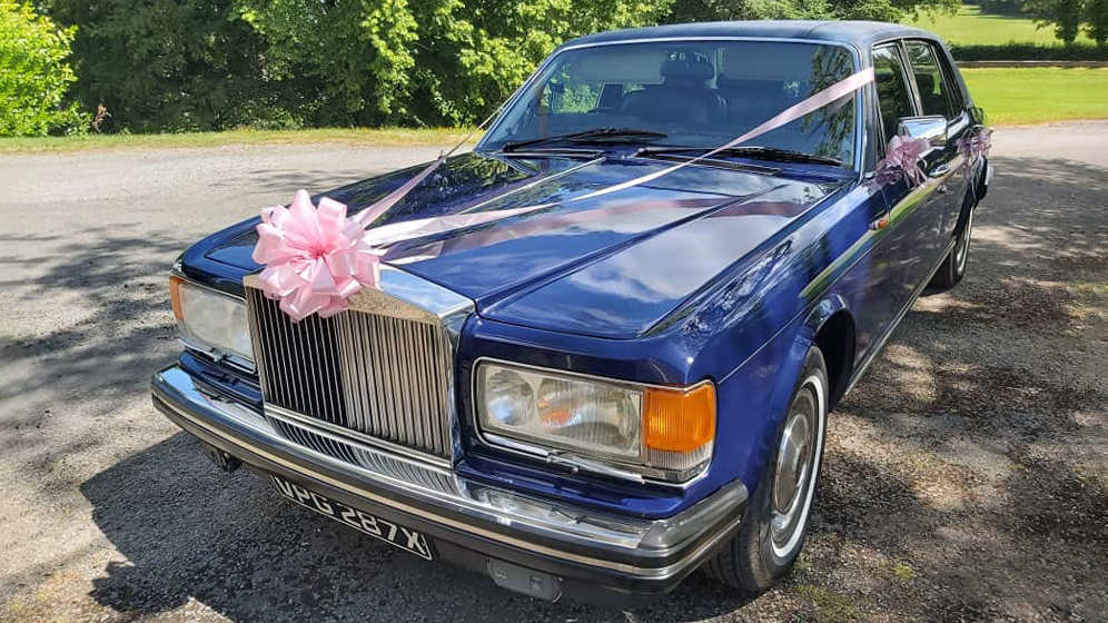 Front view of Blue Rolls-Royce Silver Spur with pink ribbon and bow across the front bonnet