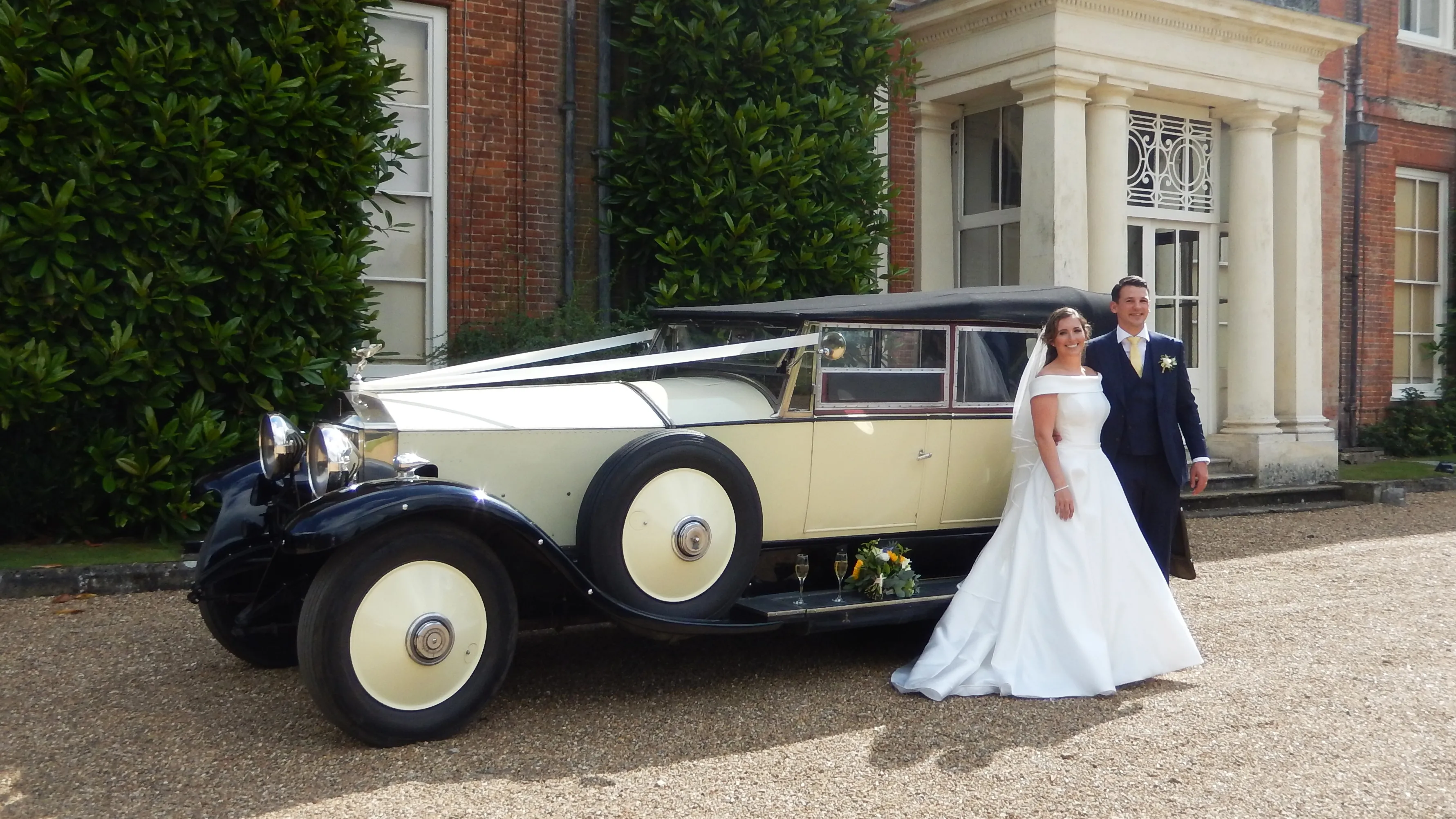 Vintage Rolls-Royce convertible with roof up decorated with traditional white wedding ribbons across its bonnet at a local Egham wedding venue. Spare wheel mounted on side skirt an