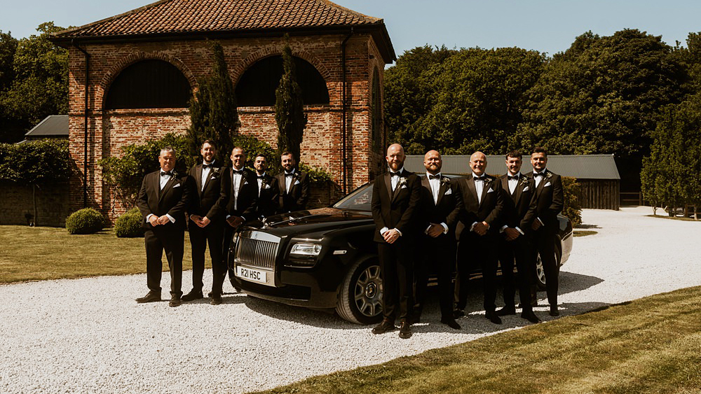Luxury Black Rolls-Royce Ghost at a wedding venue with Grooms and his groosmen all perfectly lined up on both side of the vehiclefacing towards the photographer.